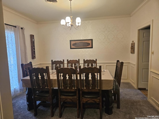 carpeted dining space with a wainscoted wall, visible vents, a decorative wall, an inviting chandelier, and ornamental molding