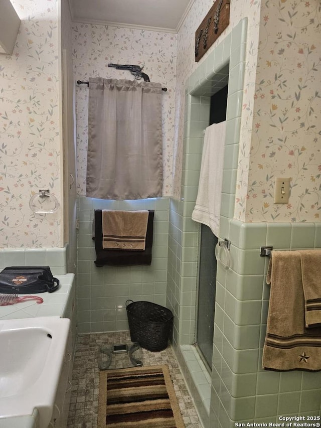 full bath with a wainscoted wall, a sink, tile walls, and wallpapered walls