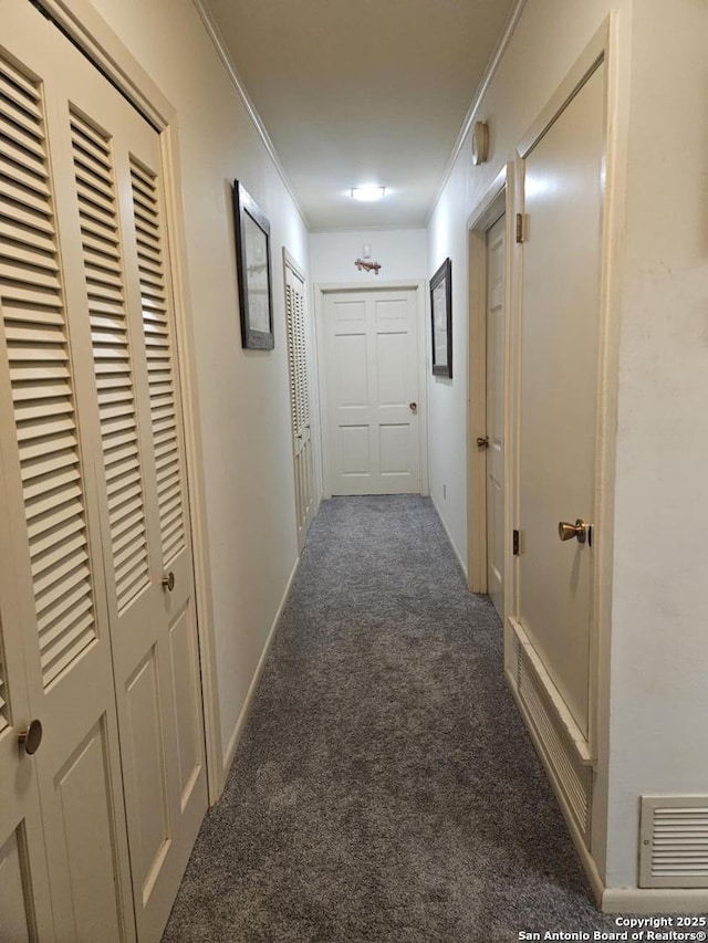 hallway with carpet floors, visible vents, ornamental molding, and baseboards