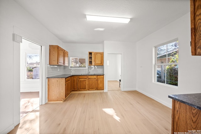 kitchen featuring a sink, baseboards, light wood-style floors, brown cabinets, and tasteful backsplash