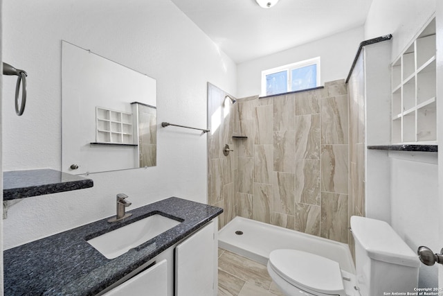 bathroom with toilet, tiled shower, and vanity