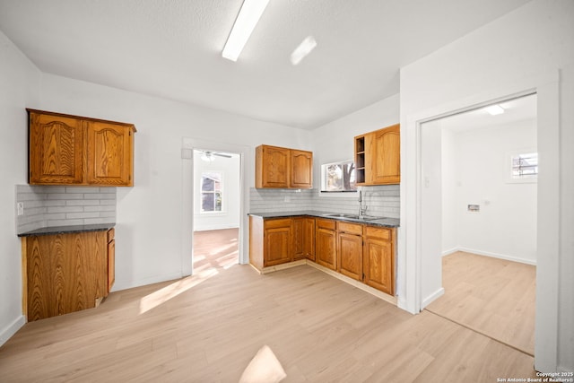 kitchen featuring brown cabinets, decorative backsplash, a sink, light wood-type flooring, and baseboards