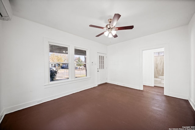 spare room featuring a wall unit AC, a ceiling fan, and baseboards