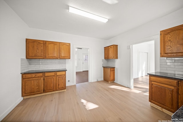 kitchen featuring light wood-style flooring, baseboards, brown cabinets, and backsplash