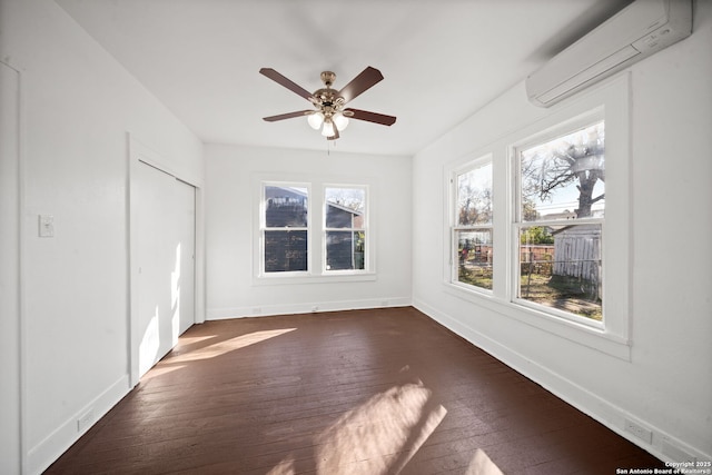 unfurnished bedroom with an AC wall unit, multiple windows, dark wood finished floors, and baseboards