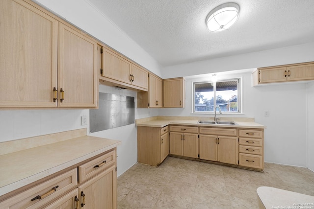 kitchen with a textured ceiling, light brown cabinets, light countertops, and a sink