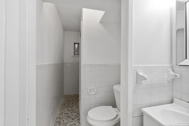 bathroom featuring toilet, a wainscoted wall, tile walls, and vanity