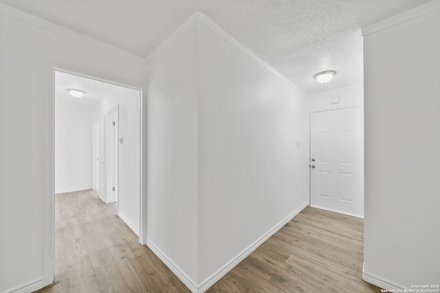 hallway with baseboards, light wood-style flooring, ornamental molding, and a textured ceiling