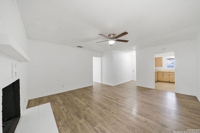 unfurnished living room featuring light wood finished floors, a brick fireplace, visible vents, and a ceiling fan