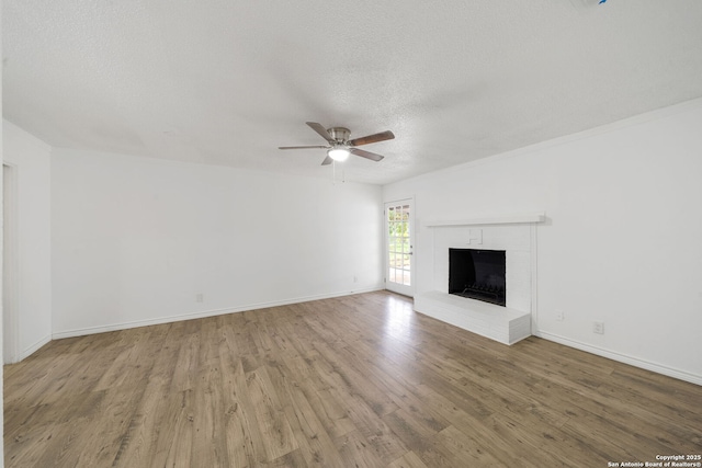 unfurnished living room with baseboards, a ceiling fan, wood finished floors, a textured ceiling, and a brick fireplace