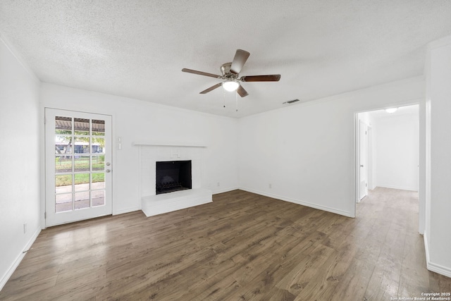 unfurnished living room with dark wood-style floors, a fireplace, visible vents, a ceiling fan, and a textured ceiling