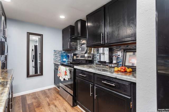 kitchen featuring tasteful backsplash, light wood-style floors, appliances with stainless steel finishes, dark cabinetry, and wall chimney range hood