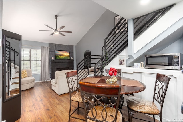 dining area featuring lofted ceiling with skylight, a brick fireplace, stairway, and wood finished floors