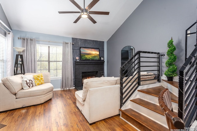 living room featuring ceiling fan, lofted ceiling, wood finished floors, stairs, and a brick fireplace