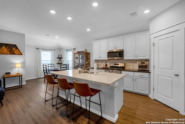 kitchen featuring stainless steel appliances, a kitchen island with sink, white cabinetry, and visible vents