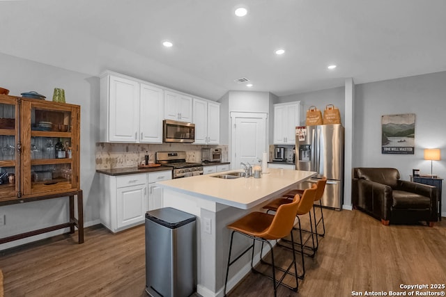 kitchen with a kitchen island with sink, a breakfast bar, a sink, white cabinetry, and appliances with stainless steel finishes