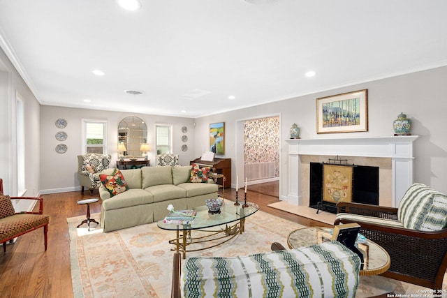 living room with baseboards, a premium fireplace, ornamental molding, light wood-type flooring, and recessed lighting