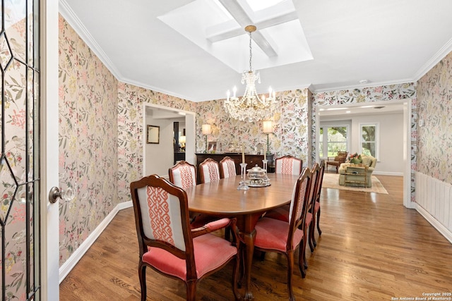 dining room with a notable chandelier, ornamental molding, wood finished floors, baseboards, and wallpapered walls