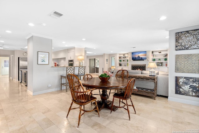 dining room featuring a warm lit fireplace, baseboards, visible vents, built in features, and recessed lighting