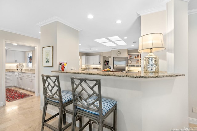 kitchen with a breakfast bar area, a peninsula, built in refrigerator, white cabinetry, and hanging light fixtures