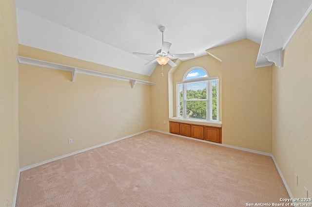 empty room featuring vaulted ceiling, baseboards, a ceiling fan, and light colored carpet