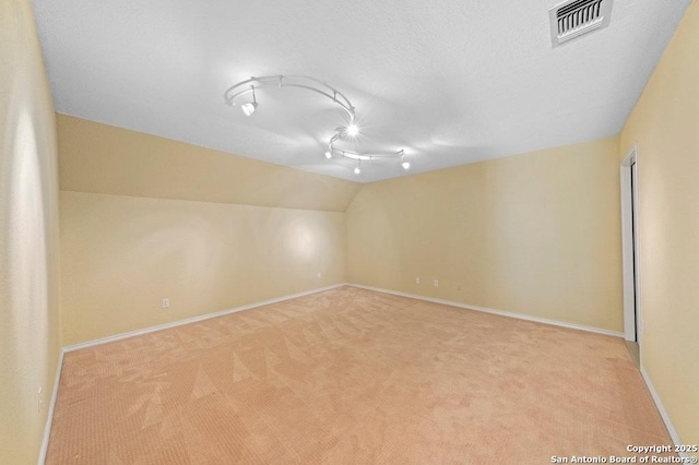 unfurnished room featuring lofted ceiling, baseboards, visible vents, and light colored carpet