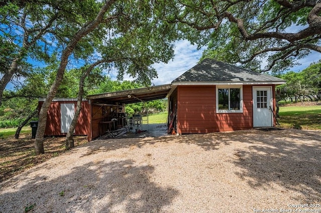 view of outdoor structure with an attached carport, driveway, and an outdoor structure