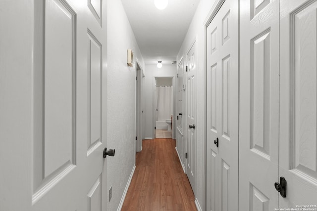 corridor featuring light wood-style flooring and baseboards