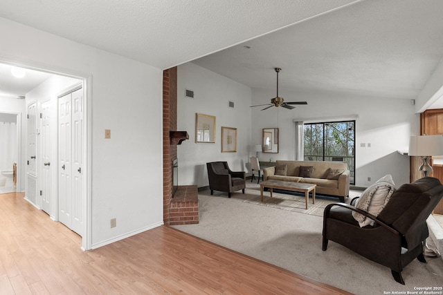 living room featuring light wood finished floors, a brick fireplace, vaulted ceiling, a textured ceiling, and ceiling fan