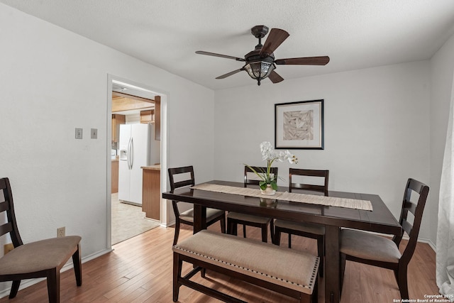 dining room with baseboards, a textured ceiling, a ceiling fan, and light wood-style floors