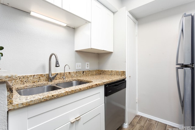 kitchen with a sink, light wood-type flooring, appliances with stainless steel finishes, and light stone counters