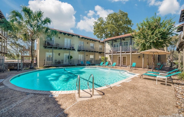 pool with french doors, fence, and a patio