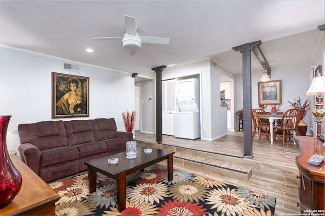 living area featuring wood finish floors, stacked washer / drying machine, visible vents, a ceiling fan, and a textured ceiling