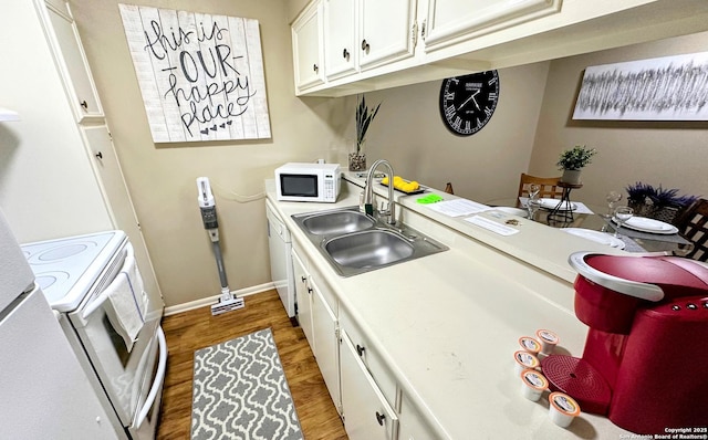 kitchen with white appliances, wood finished floors, light countertops, white cabinetry, and a sink