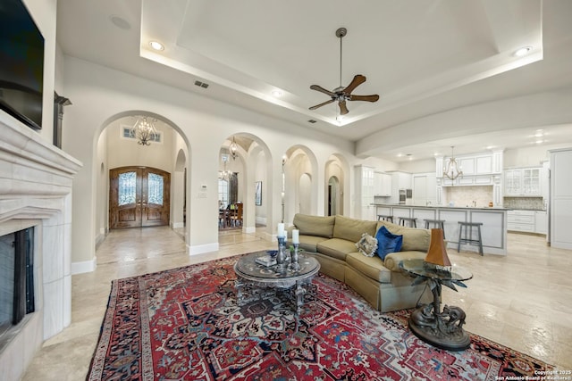 living room featuring arched walkways, ceiling fan with notable chandelier, visible vents, baseboards, and a tray ceiling