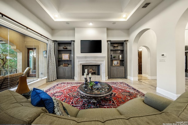 living room featuring visible vents, arched walkways, baseboards, a raised ceiling, and a lit fireplace