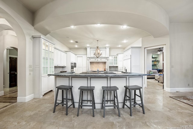 kitchen featuring glass insert cabinets, arched walkways, white cabinets, and a large island with sink