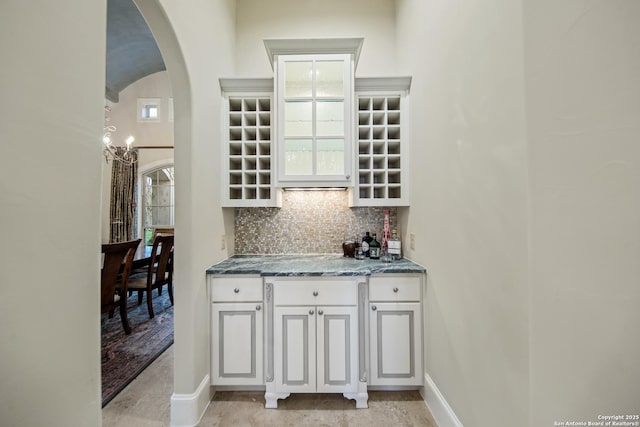 bar featuring arched walkways, baseboards, and decorative backsplash