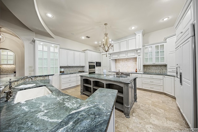 kitchen featuring glass insert cabinets, decorative light fixtures, a sink, and dark stone countertops