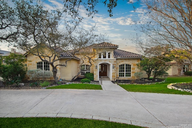 mediterranean / spanish-style home featuring stone siding, a tile roof, and a front lawn