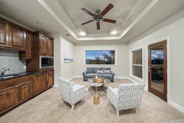 living area with light carpet, a raised ceiling, and baseboards