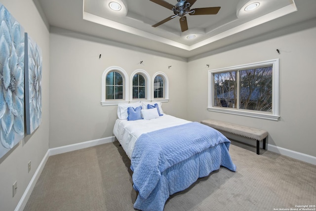 carpeted bedroom with baseboards and a raised ceiling