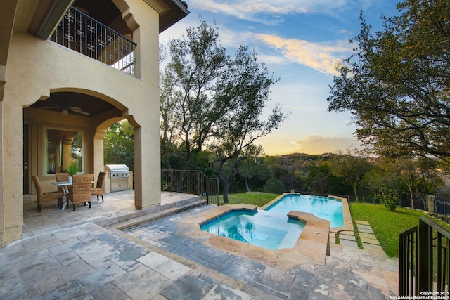 pool at dusk featuring a yard, area for grilling, a patio, and an outdoor kitchen