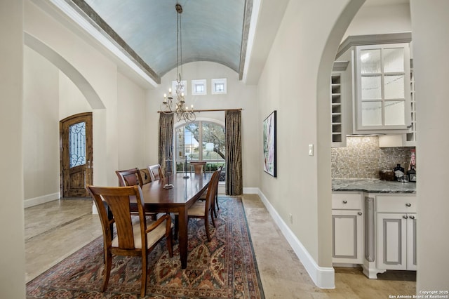 dining room with a notable chandelier, baseboards, vaulted ceiling, and arched walkways