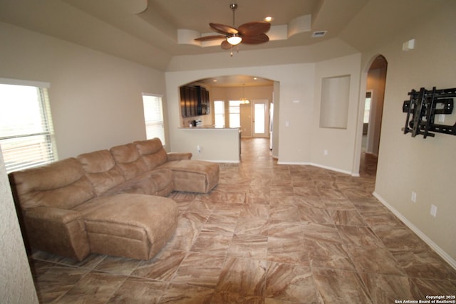 living room with arched walkways, a ceiling fan, visible vents, baseboards, and a raised ceiling