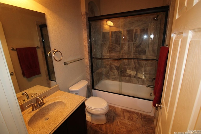 bathroom featuring a textured wall, vanity, toilet, and bath / shower combo with glass door