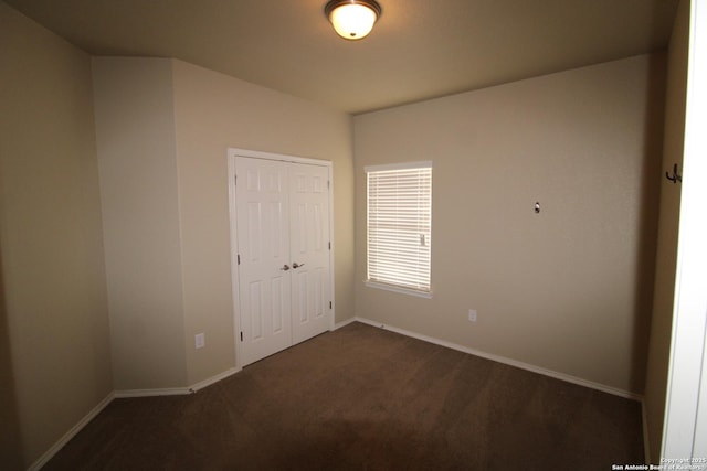 unfurnished bedroom with a closet, dark carpet, and baseboards