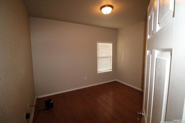 spare room with baseboards and dark wood-type flooring