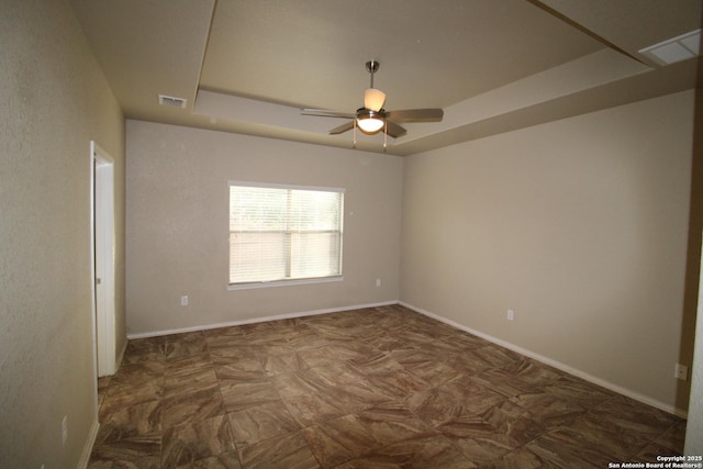 unfurnished room with a ceiling fan, a tray ceiling, visible vents, and baseboards