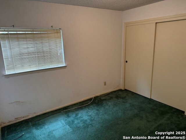 unfurnished bedroom with a textured ceiling, dark colored carpet, and a closet